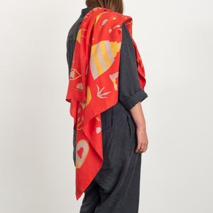 El Sueño scarf in red, draped across a model's shoulder to give a sense of drape and scale. Model is wearing a charcoal linen overall.